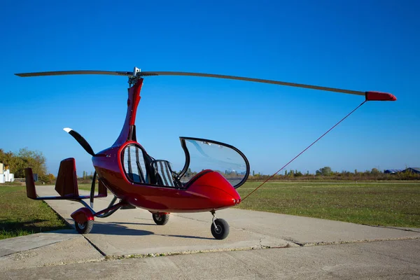 Kırmızı otojiroskop güneşli bir günde havaalanına park etmiş. Gökyüzüne karşı jiroskopter.