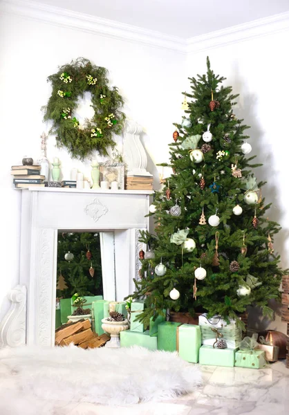Süslü köknar ağacı ve beyaz oturma odasındaki şöminenin yanında hediye kutuları. Dikey Noel dekore edilmiş iç dekorasyonu