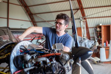 Avia yağını küçük bir uçakla kontrol eden bir adam. Uçak hangarda. Uçak motorunun yanında aletleri tutan tamirci. Küçük havacılık.