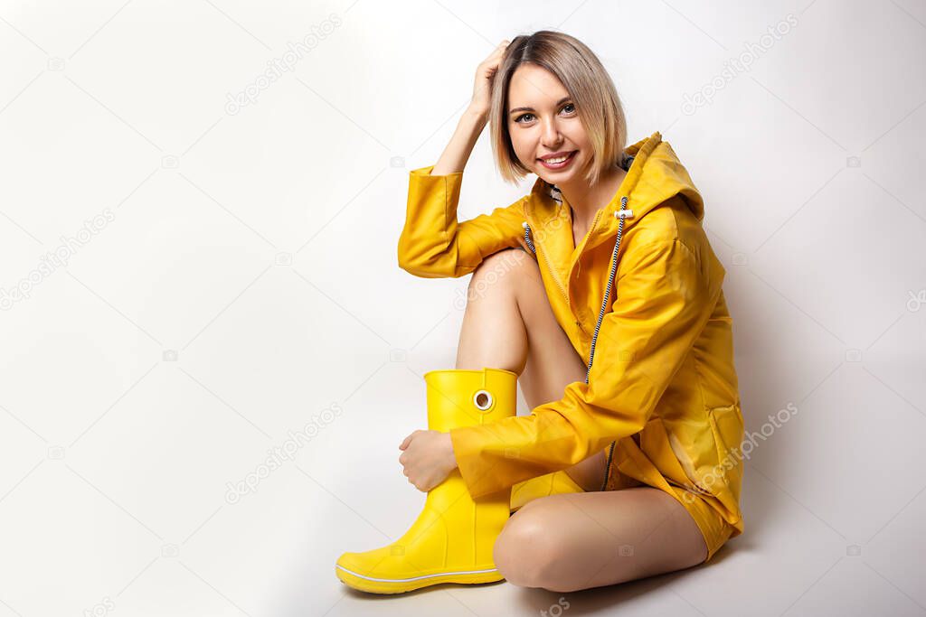 Young woman sitting and smiling in yellow slicker and rubber boots
