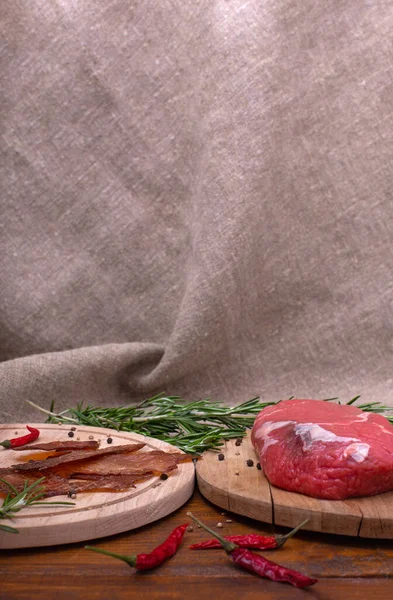 糊状的肉和生牛肉在木制桌子上的圆形木板上 在牛皮纸的背景前 有复制的空间 烹调肉类小吃的配料 迷迭香 红辣椒和胡椒玉米 垂直方向 图库照片