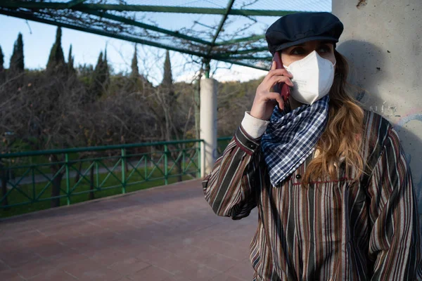 Maskeli kız parkta telefonla konuşuyor..