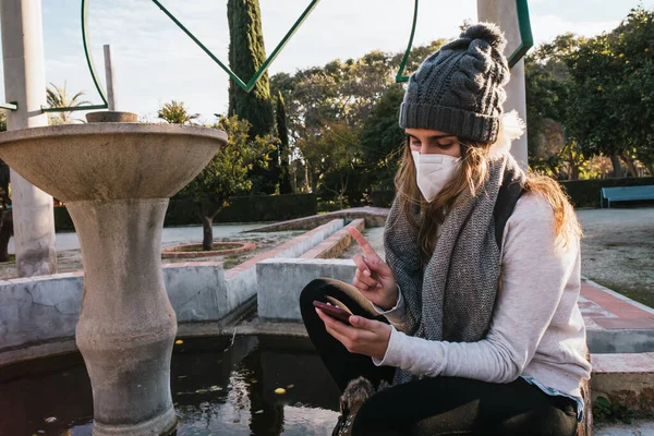 Parkta maskeli bir kız cep telefonuyla sohbet ediyor..