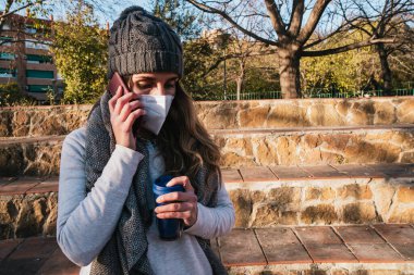 Maskeli kız parkta telefonla konuşuyor..