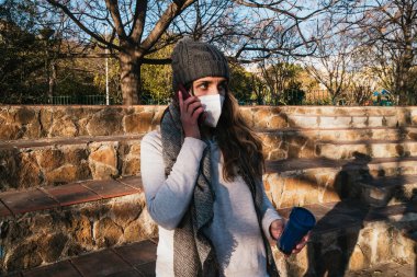 Maskeli kız parkta telefonla konuşuyor..