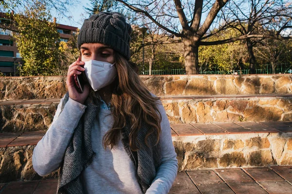 Maskeli kız parkta telefonla konuşuyor..