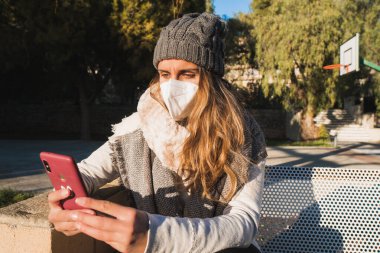 Parkta maskeli bir kız cep telefonuyla sohbet ediyor..