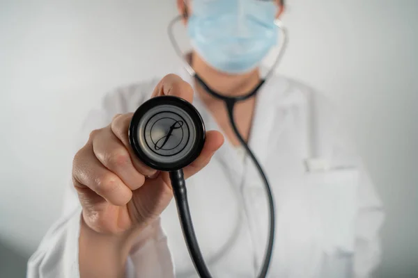 Hasta kalbini dinlemek için fonendoskoplu maskeli bir doktor..