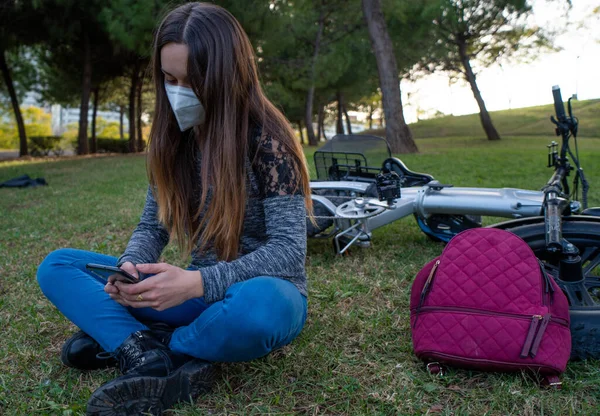 Parkta cep telefonu olan maskeli bir kız..