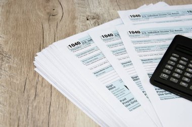Tahta bir masanın üzerinde hesap makinesi olan 1040 vergi formu. Mali belge.