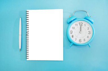 Mavi çalar saat, beyaz boş not defteri ve kalem. Mavi arka plan. Yukarıdan görüntüle.