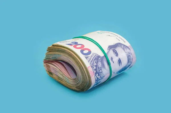 Mavi arka planda izole edilmiş elastik bir bantla bağlanmış Ukrayna Hryvnia 'sı. Para yığını. Finansal konsept. 200 Hryvnia banknotları yuvarlandı..