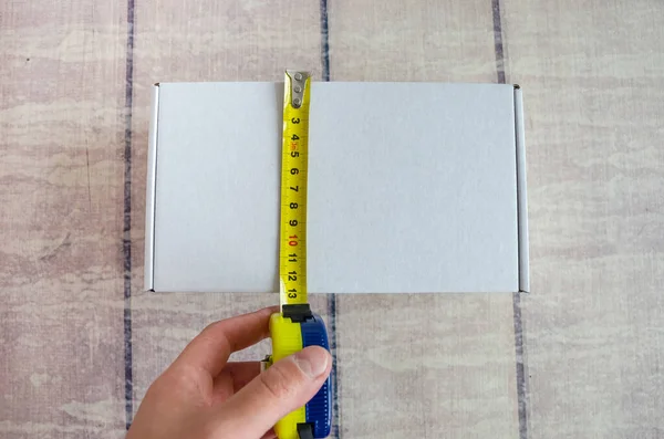 Worker\'s hand using a tape measure measures cardboard boxes. Shopping lifestyle in warehouse concept.Measuring box concept. Cardboard boxes and tape measure in hand on a wooden background.