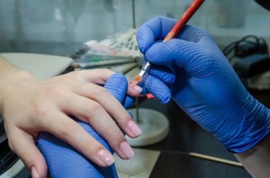 Güzellik uzmanının yakın çekimi bir kuaför salonundaki müşterisine renkli oje sürüyor. Çivi bakımı konsepti. Profesyonel manikür..