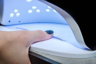 Müşteri lamba lambası jöle cilası manikür sürecinde bir tırnağı kurutuyor. Salon prosedürü.