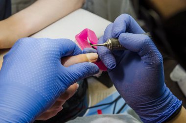 Tırnak tedavisi, güzellik salonunda bileme ve cilalama. Profesyonel güzellik uzmanının yakın çekimi. Siyah eldivenli eller. Müşteri kadın tırnaklarının elektrikli matkap dosyası üzerinde çalışıyor..