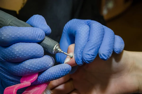 美容室での指の爪の治療 研削と研磨 クライアントの女性の指の爪に電気ドリルファイルで作業黒手袋でプロのマスター美容師の手のクローズアップ — ストック写真