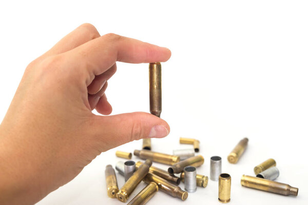 hand holds an empty cartridge case with two fingers. White background, close-up.