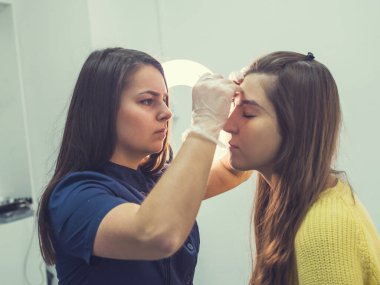 Usta makyajı düzeltir, iplikle şekillendirir ve güzellik salonunda kaşlarını cımbızla yolar. Profesyonel yüz bakımı..