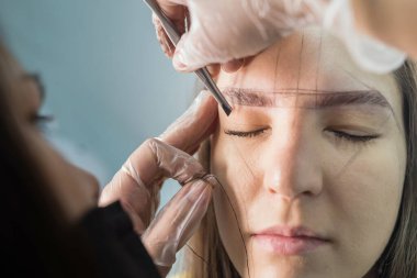 Usta makyajı düzeltir, iplikle şekillendirir ve güzellik salonunda kaşlarını cımbızla yolar. Profesyonel yüz bakımı..