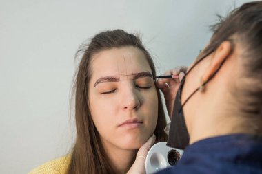 Genç ve güzel bir bayan usta müşteriye kaş düzeltme prosedürü uygular. Güzellik salonunda kaş boyama konsepti.