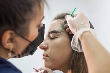 Genç ve güzel bir bayan usta müşteriye kaş düzeltme prosedürü uygular. Güzellik salonunda kaş boyama konsepti.