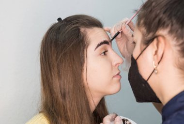 Genç ve güzel bir bayan usta müşteriye kaş düzeltme prosedürü uygular. Güzellik salonunda kaş boyama konsepti.