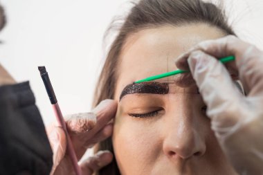 Genç ve güzel bir bayan usta müşteriye kaş düzeltme prosedürü uygular. Güzellik salonunda kaş boyama konsepti.