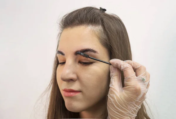 The hand of the master applies anesthetic cream to the eyebrows before the permanent makeup procedure with a brush. Eyebrow dyeing concept.