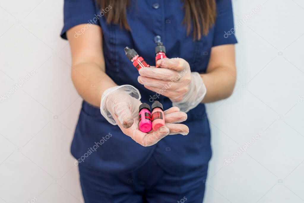 Young woman cosmetologist holds bottles for permanent makeup and eyebrow tattoo.