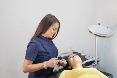 Güzellik salonundaki bir prosedür sırasında güzellik uzmanı ve müşteri. Usta bir kızda kalıcı makyaj ve kaş kaplaması için bir cihaz vardır..