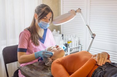 Kozmetik uzmanı pamuklu ped kullanan genç bir kadının yüzünü temizliyor. Kozmetik ürünleri hijyenik disklerle kaldırılıyor.