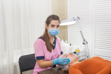 Kozmetik uzmanı pamuklu ped kullanan genç bir kadının yüzünü temizliyor. Kozmetik ürünleri hijyenik disklerle kaldırılıyor.