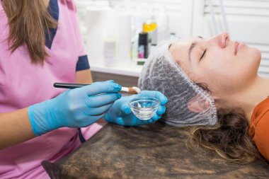 Güzellik uzmanı yüz maskesi takıyor. Genç bir kız kanepede yatıyor. Güzellik salonunda kozmetik prosedürleri.