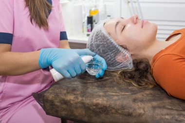 Güzellik uzmanı yüz maskesi hazırlıyor. Genç kız kanepede yatıyor. Güzellik salonunda kozmetik prosedürleri.