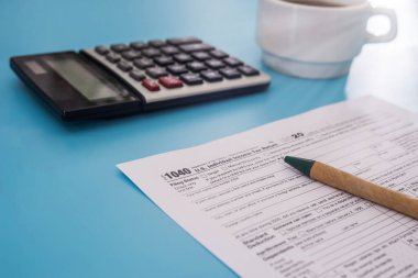 Vergi konsepti. Hesap makinesi, kalem ve kahve fincanı ile mavi arka planda Amerikan vergi formu. Nisan ayında doldurmak için 1040 form. Vergi zamanı.