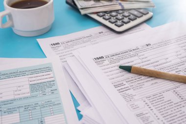 Vergi konsepti. Hesap makineli Amerikan vergi formu, mavi arka planda kalem ve dolar. Nisan ayında doldurmak için 1040 form. Vergi zamanı.