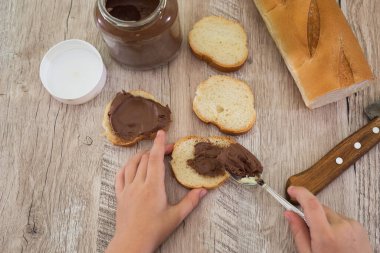 Elleri bir baget ekmeğe çikolata ezmesi sürüyor. Ahşap arkaplan.