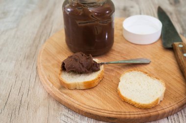 Bir kavanoz çikolatalı fındık ezmesi ve tahta arka planda baget dilimleri..