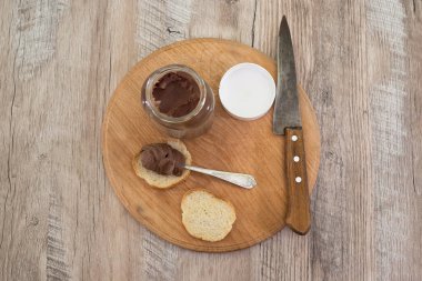 Bir kavanoz çikolatalı fındık ezmesi ve tahta arka planda baget dilimleri..