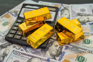 Hesap makineli altın çubuklar ve siyah arkaplanda dolar.