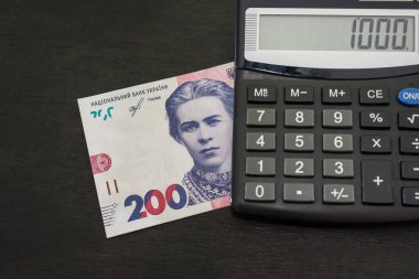200 Hryvnia 'lık yeni banknot ve siyah ahşap arka planda bir hesap makinesi. Yakın plan..