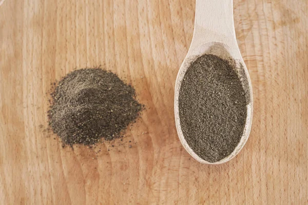 black ground pepper in a wooden spoon on a wooden background. A pile of ground pepper. View from above.