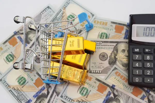 gold bars in a shopping cart and a calculator on the background of dollars. View from above.
