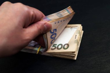 Kadın eli, siyah arka planda bir deste içinde Hryvnia 'yı sayar. Yakın plan..