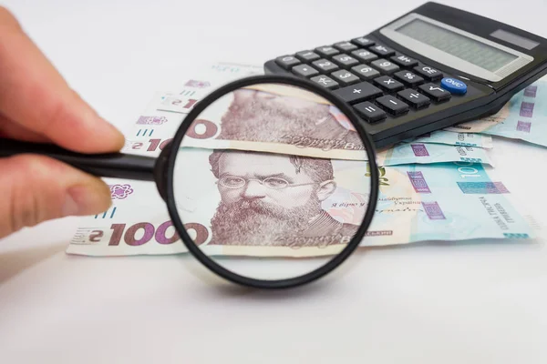 Elinde büyüteç olan el 1000 Hryvnia Ukrayna parası kontrol ediyor. Mali konsept.