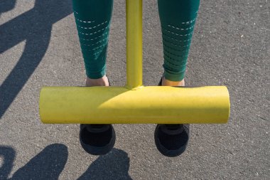 Kadın bacakları temiz havada simülatör üzerine eğitilir. Sporcunun bacakları dambılı kaldırsın..