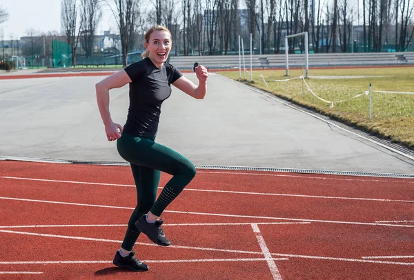 Stadyumda kameraya gülümseyen bir kadın koşuyor. Yaz fitness antrenmanı. Koşmak, spor, sağlıklı aktif yaşam tarzı.