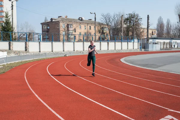 A woman runs on the track of the stadium. Summer fitness workout. Running, sports, healthy active lifestyle.