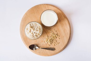 Beyaz arka planda tahta bir tahtanın üzerinde bir bardak sütle bir kasede yulaf ezmesi. Sağlıklı ve besleyici bir sabah kahvaltısı. Yukarıdan görüntüle.